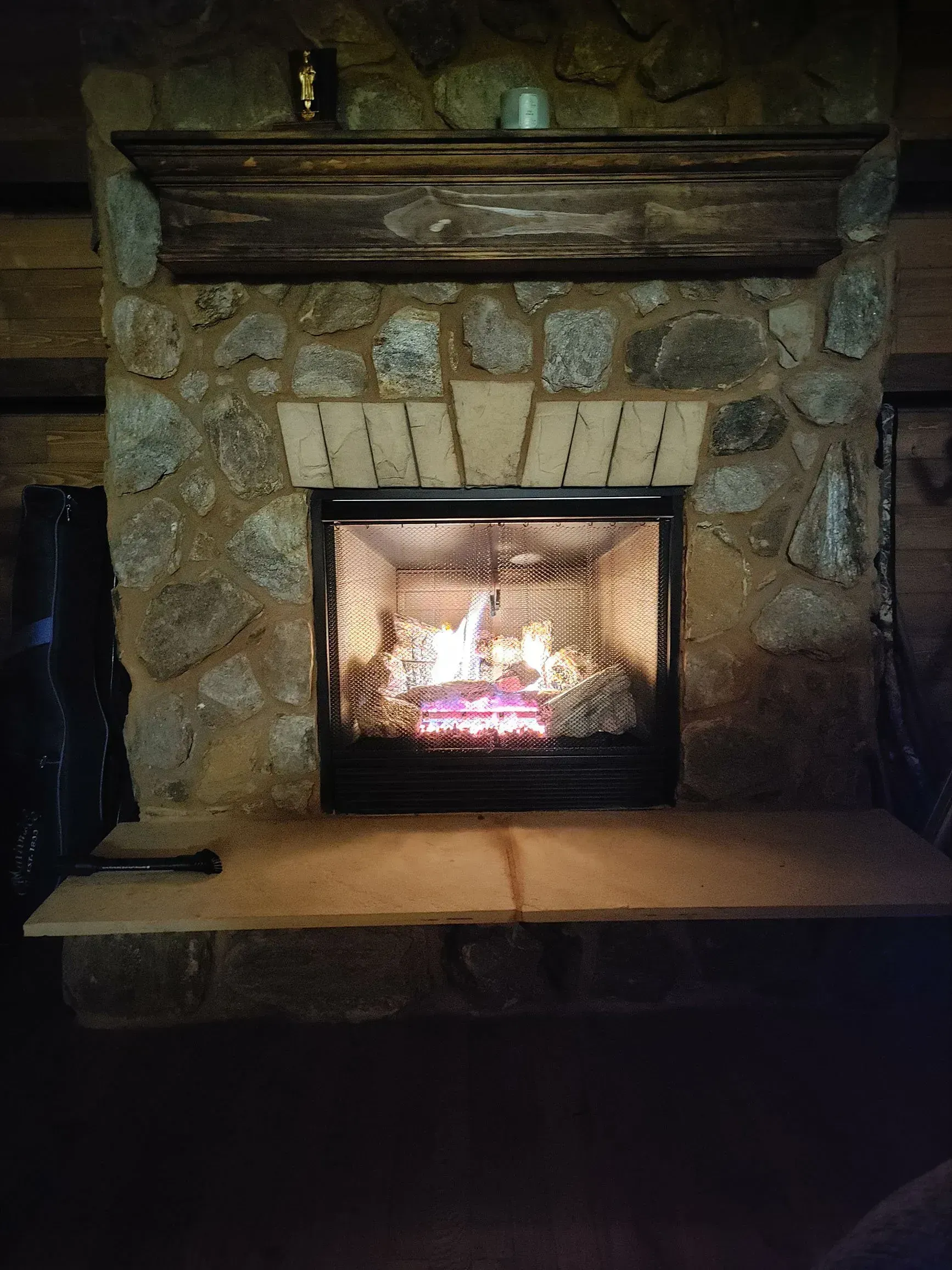 Fireplace with lit fire inside a stone surround, wooden mantel.