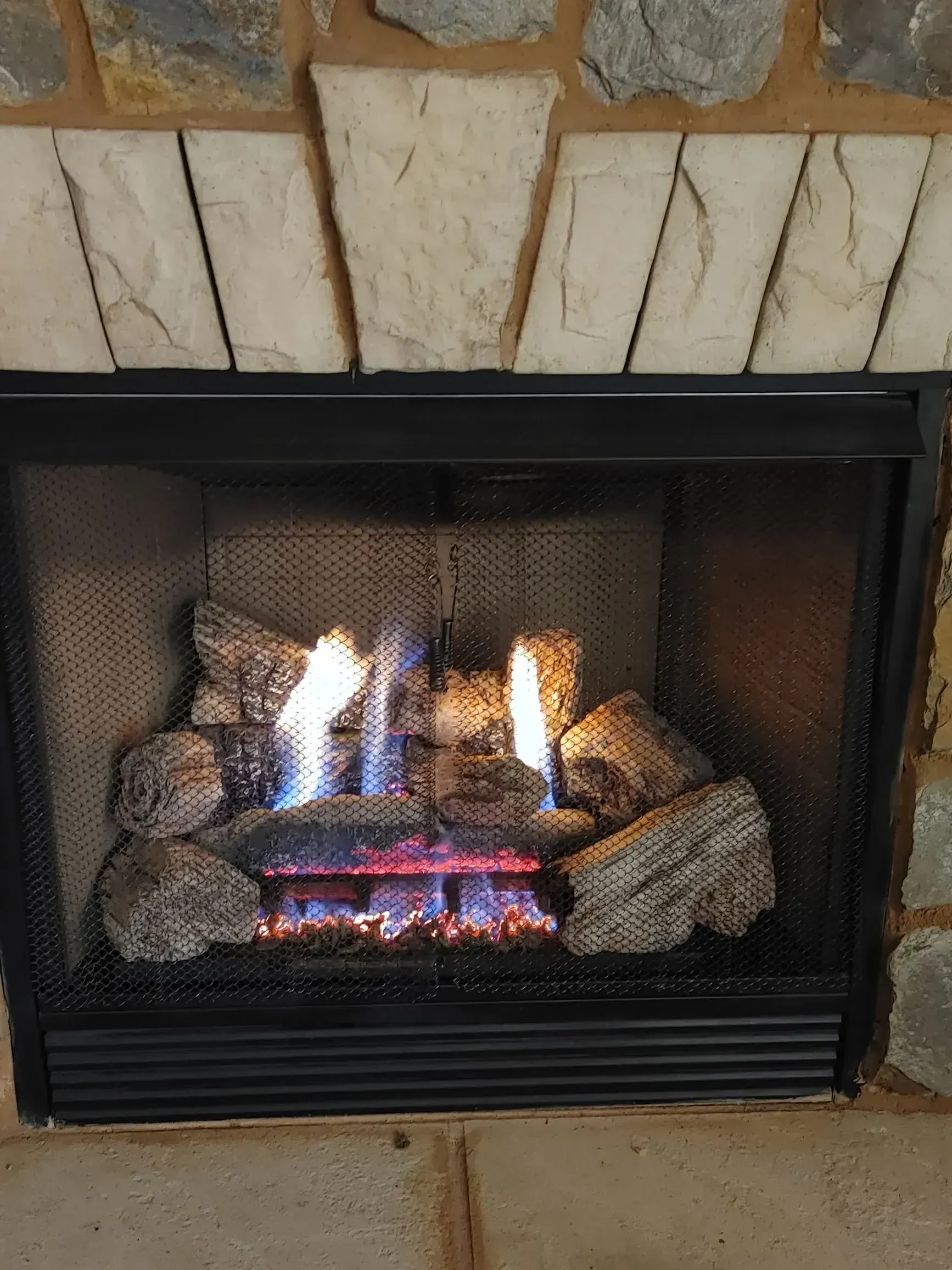 Gas fireplace with blue and orange flames, surrounded by gray rocks and stone facade.