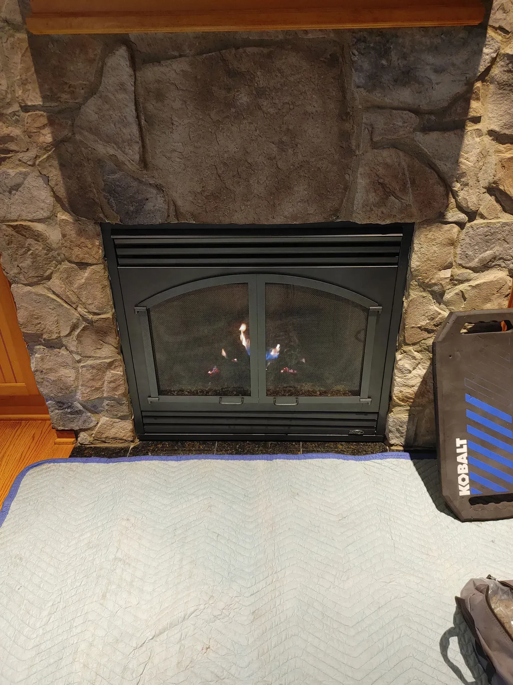 Fireplace with stone surround, flames visible behind a black mesh screen.