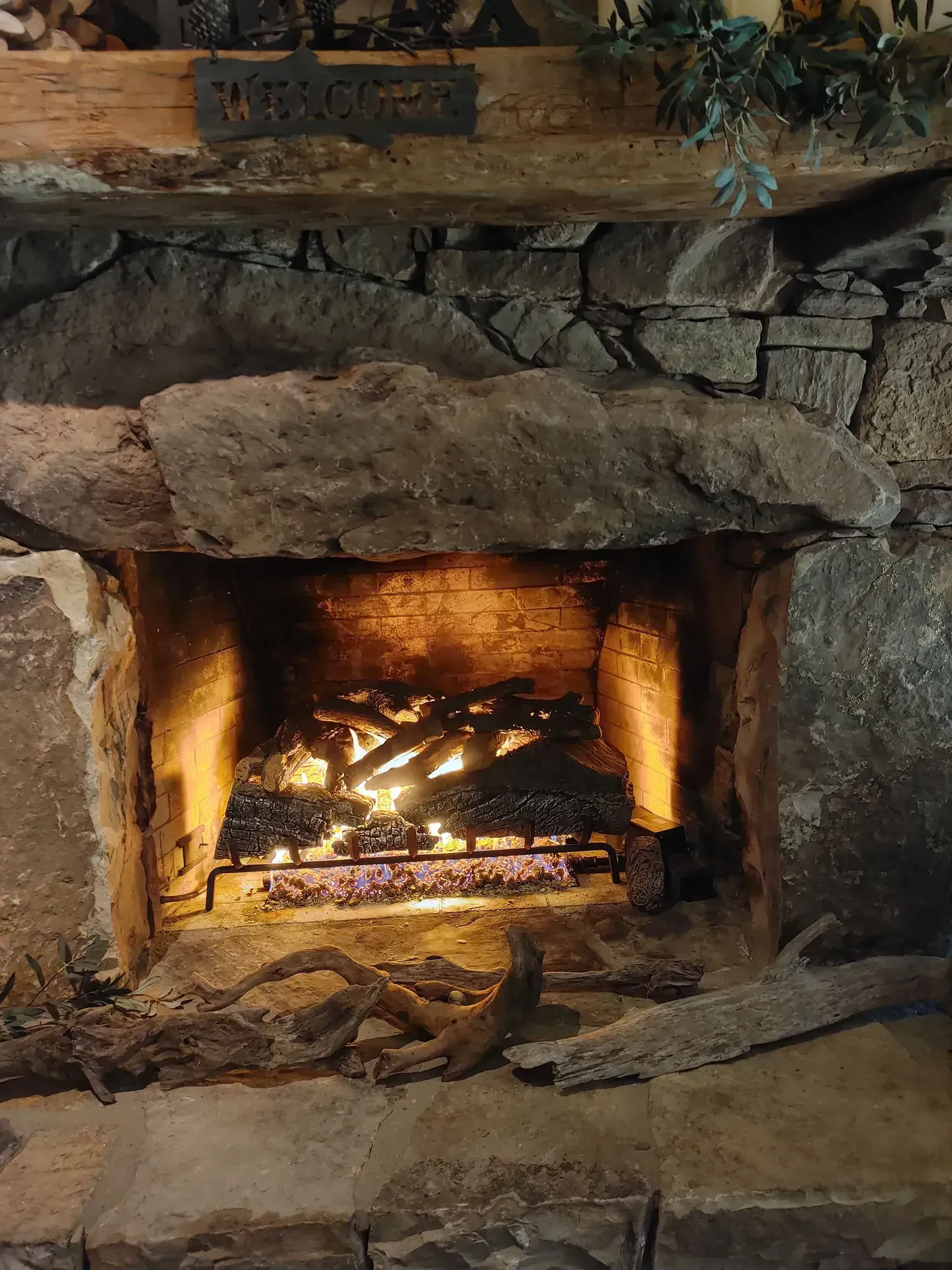 Fireplace with burning logs, built with stone and a wooden beam mantel.