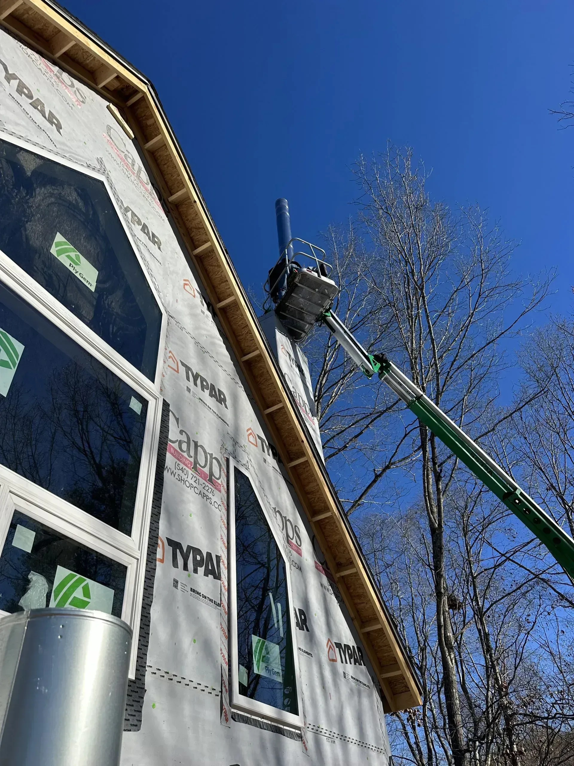 Construction worker in lift, working on a house with Tyvek siding on a sunny day.