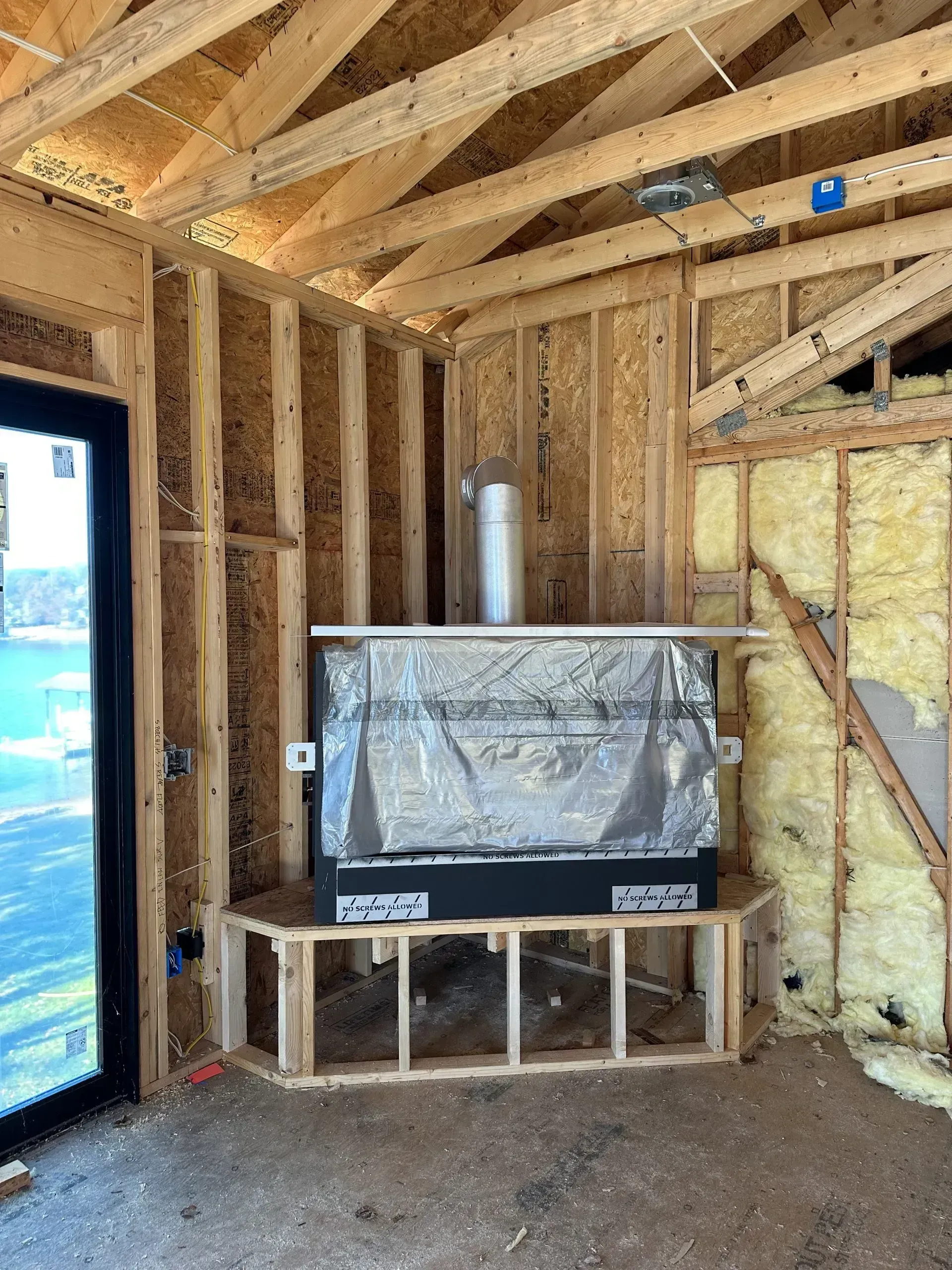 Interior of a room under construction with a built-in fireplace. Framing, insulation, and chimney visible.