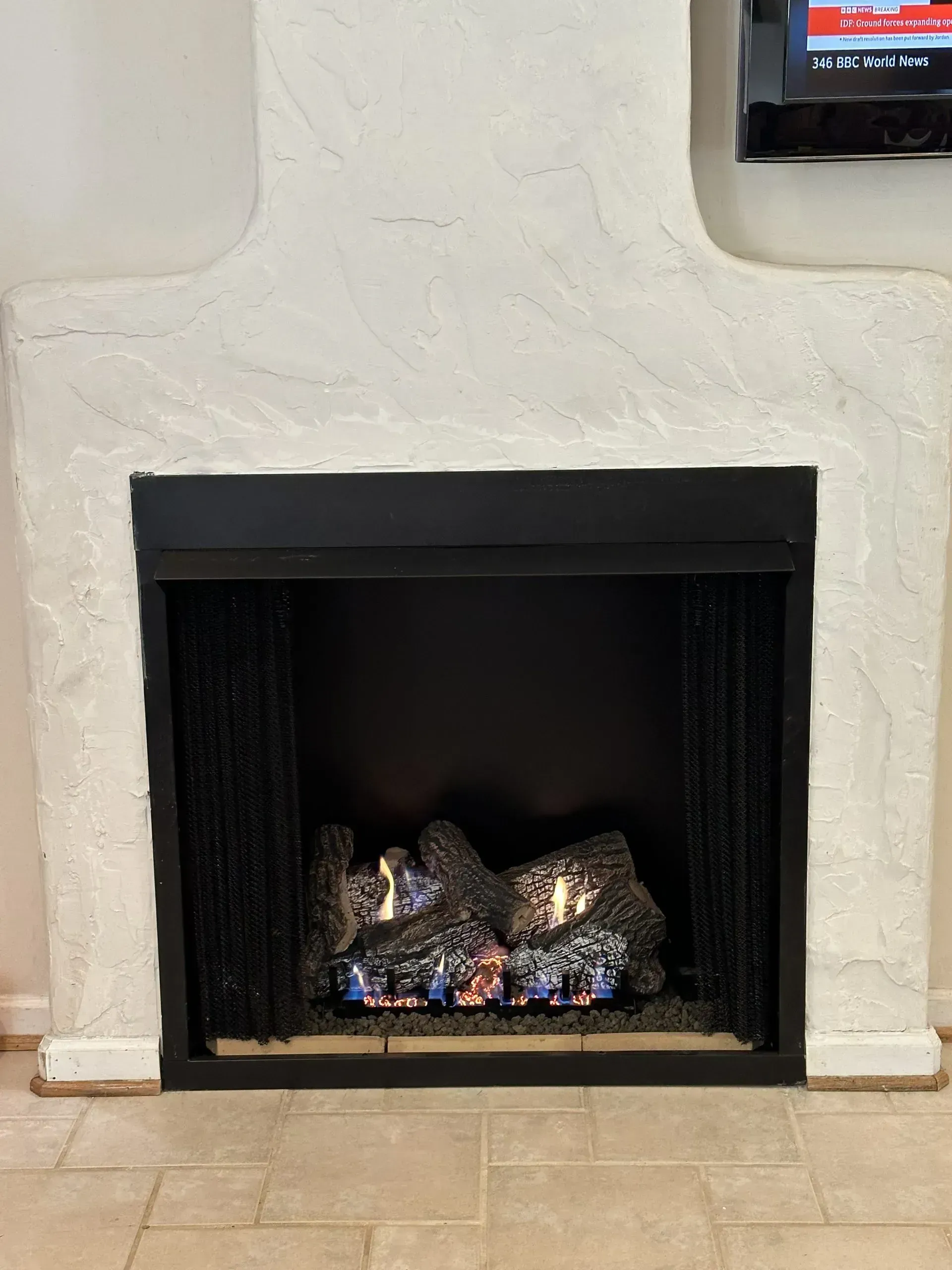 Fireplace with white stucco surround; black interior, flames visible.