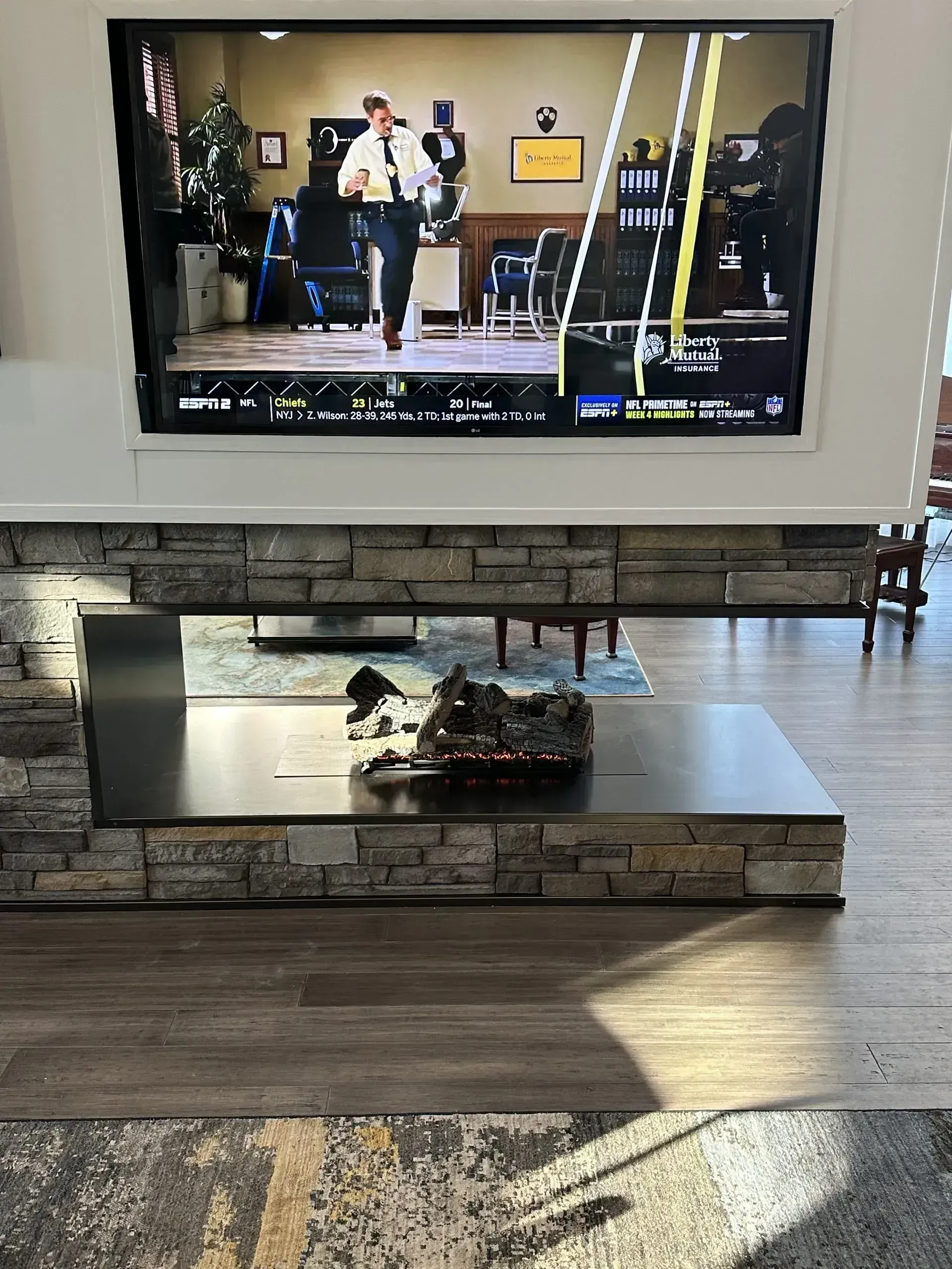 TV screen showing a person running, mounted above a fireplace with stone and a dark hearth.
