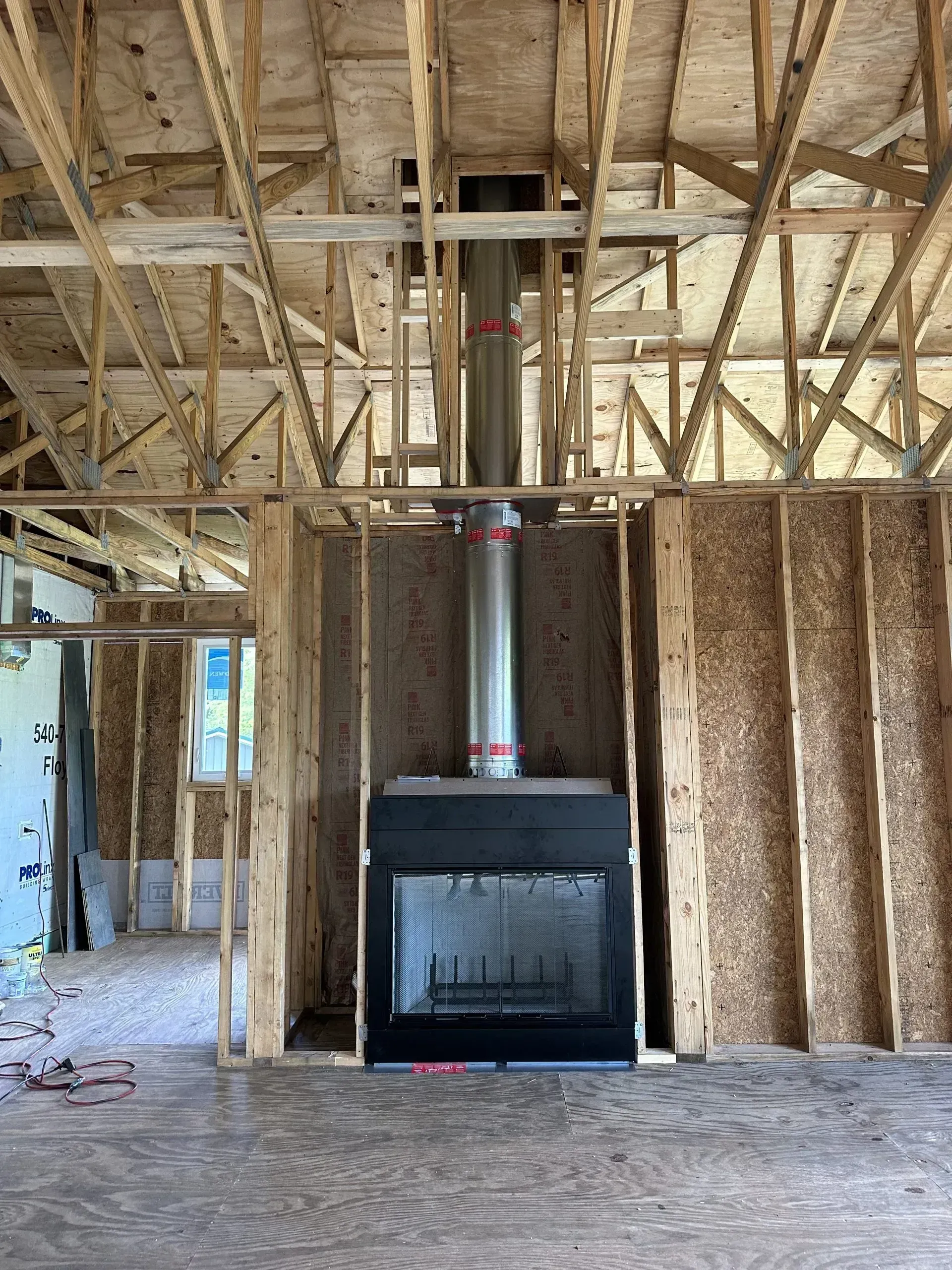 Interior of a house under construction. A black fireplace with metal chimney pipe is framed by wooden studs.