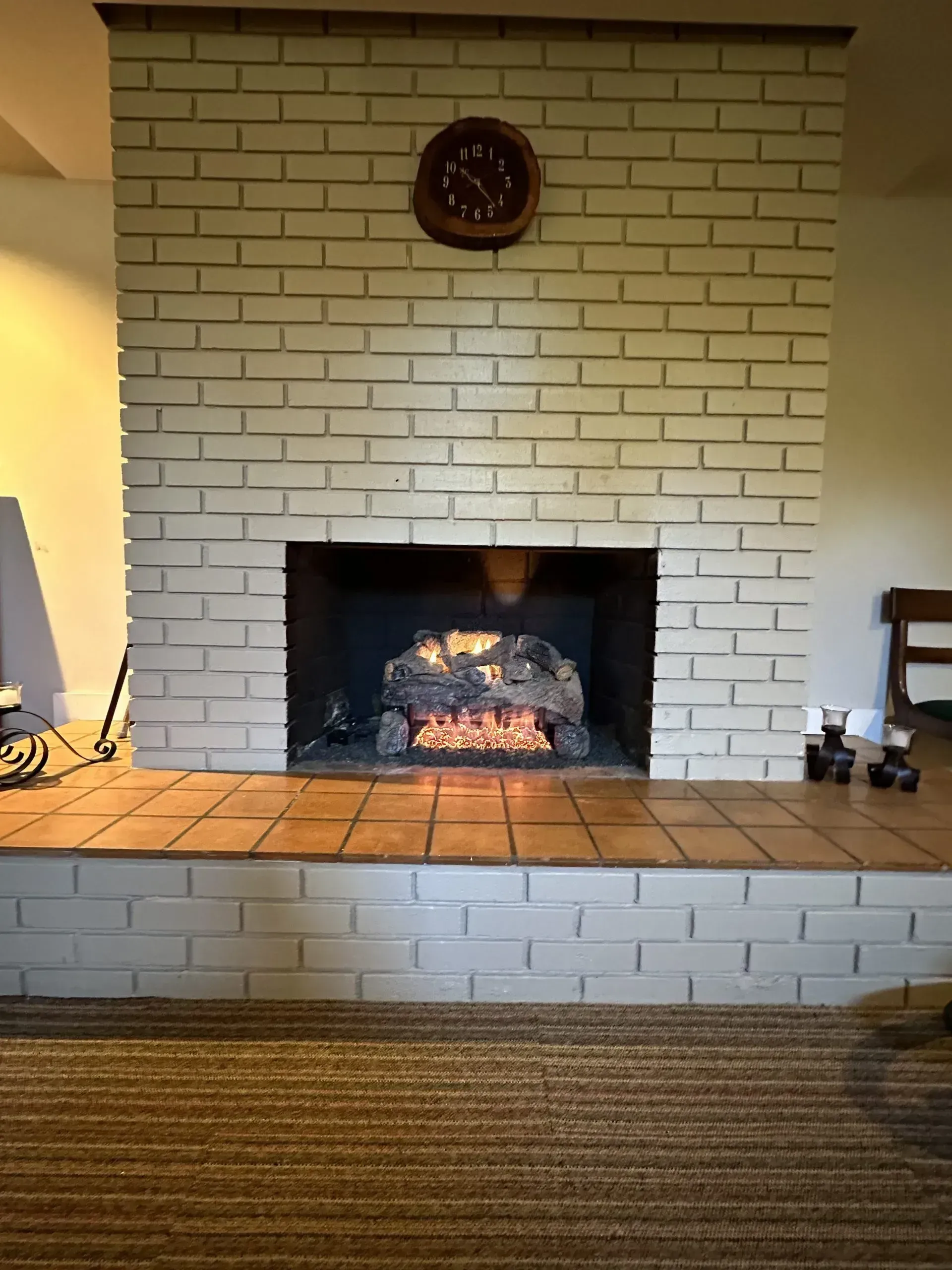 Brick fireplace with an electric fire, tile hearth, and a clock on the brick wall.