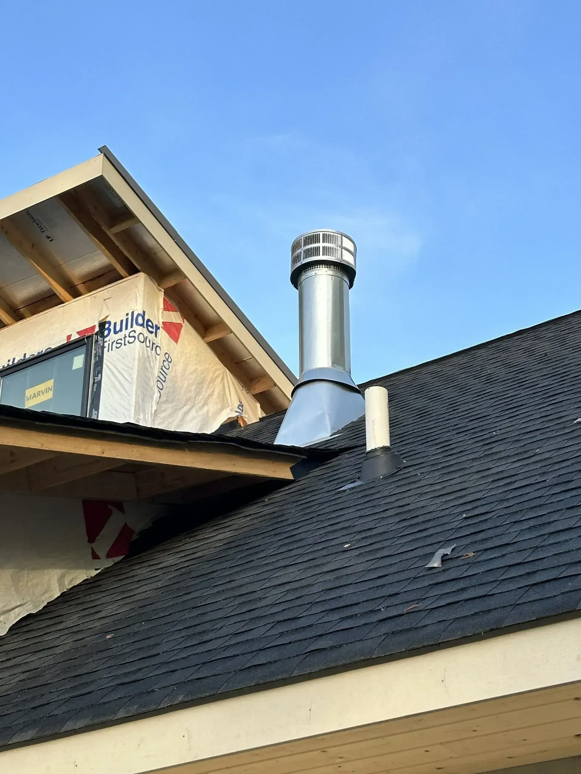 Chimney on a roof, near a roof under construction, against a blue sky.