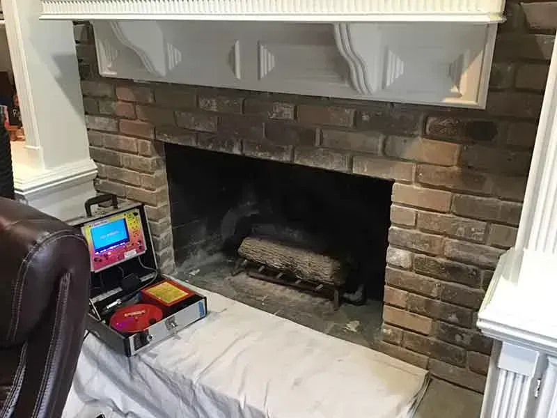 Fireplace with exposed brick and white mantel; a device sits on the hearth, partially covered in white sheeting.