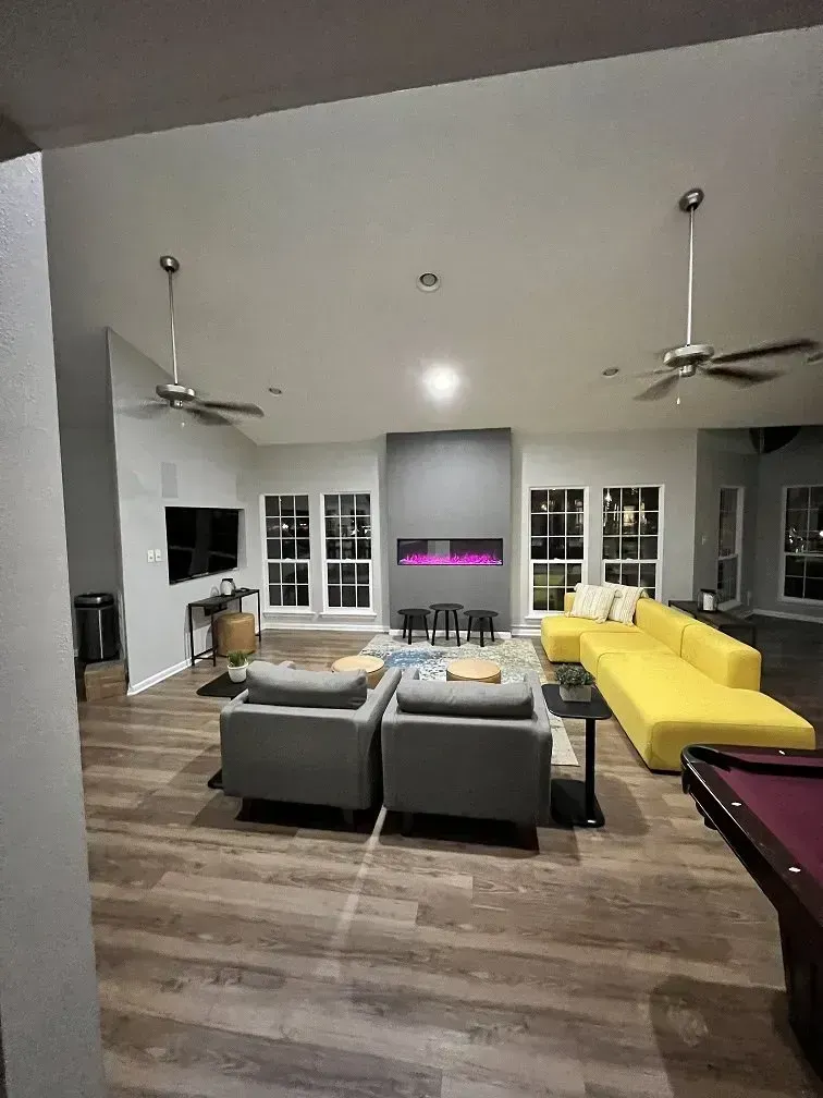 Modern living room with yellow couch, gray chairs, fireplace, TV, and pool table.