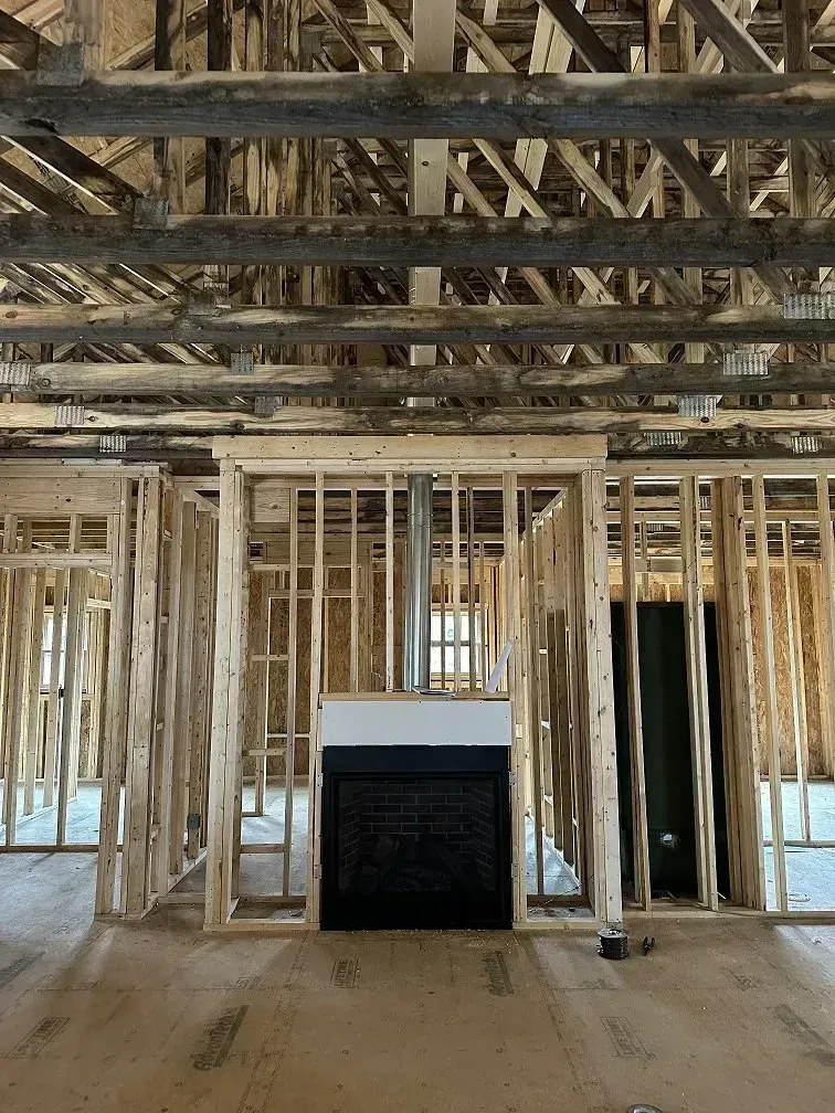 Interior framing of a house under construction with a fireplace and exposed roof beams.