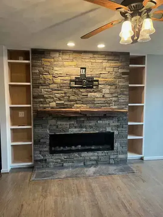 Fireplace with stone surround, flanked by white bookshelves, mounted TV above, and wooden mantle.