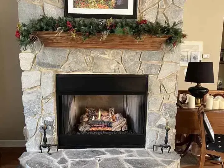Stone fireplace with gas logs, decorated with garland and a wooden trough.