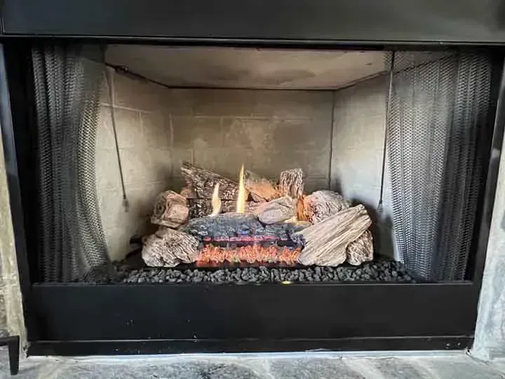 Gas fireplace with burning flames, artificial logs, and black mesh screens.