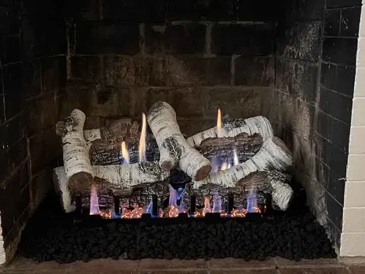Gas fireplace with birch logs and flames. Black brick surround.