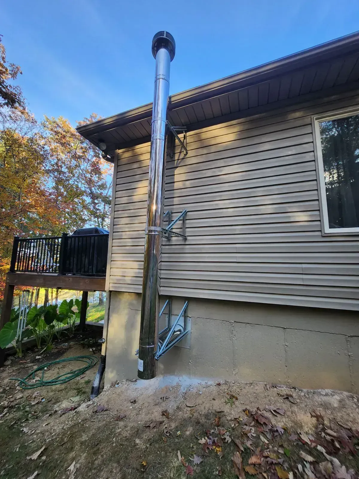 Exterior view of a house with a tall, silver chimney. The chimney extends from a brick foundation.