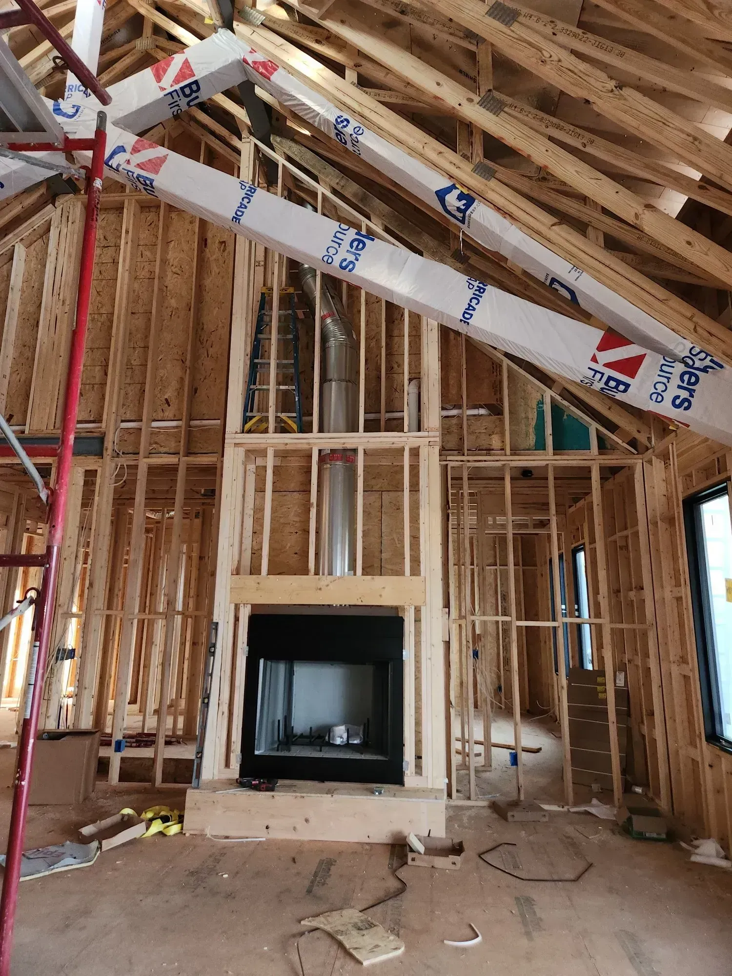 Interior framing of a house under construction, with a fireplace, chimney, and exposed wooden beams.