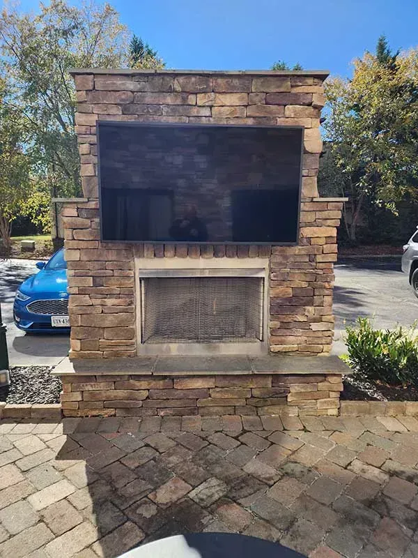 Outdoor stone fireplace with a built-in television above the firebox, set on a brick patio.