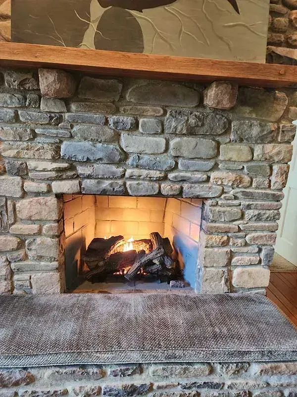 Stone fireplace with burning logs, wooden mantel, and a stone hearth.
