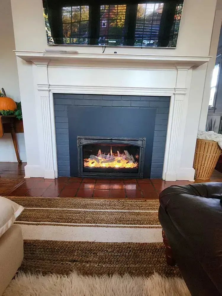 Fireplace with lit flames, framed by a white mantel. A TV hangs above.