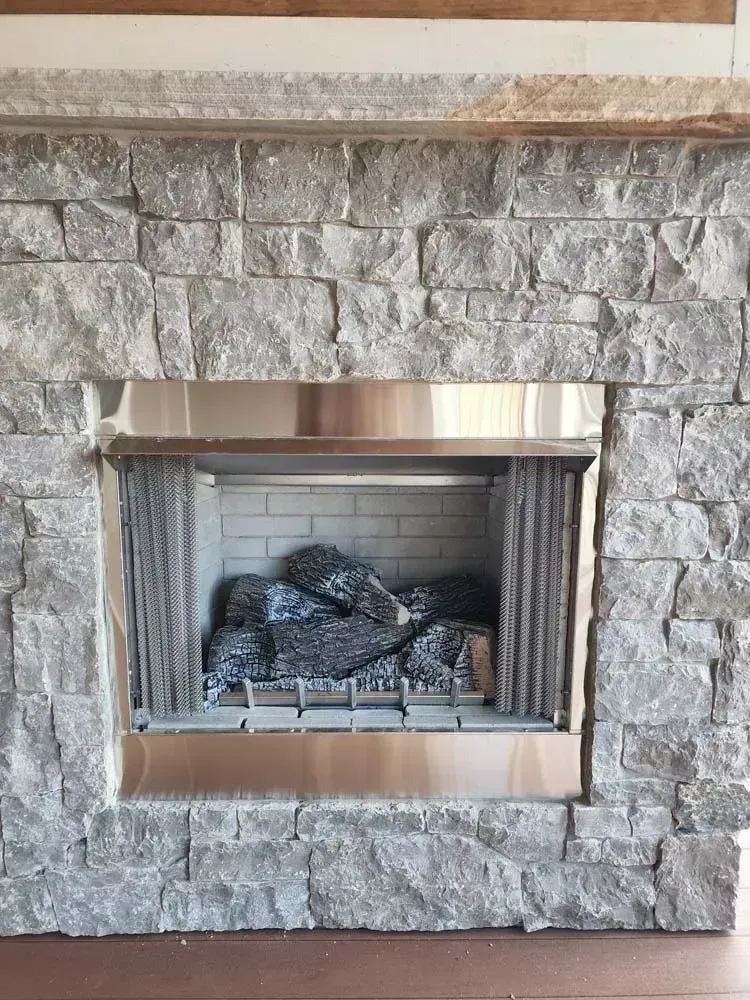 Fireplace with gray stone surround and stainless steel trim. Logs inside.