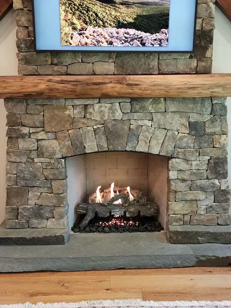 Stone fireplace with a burning fire, a wooden mantel, and a mounted TV above.