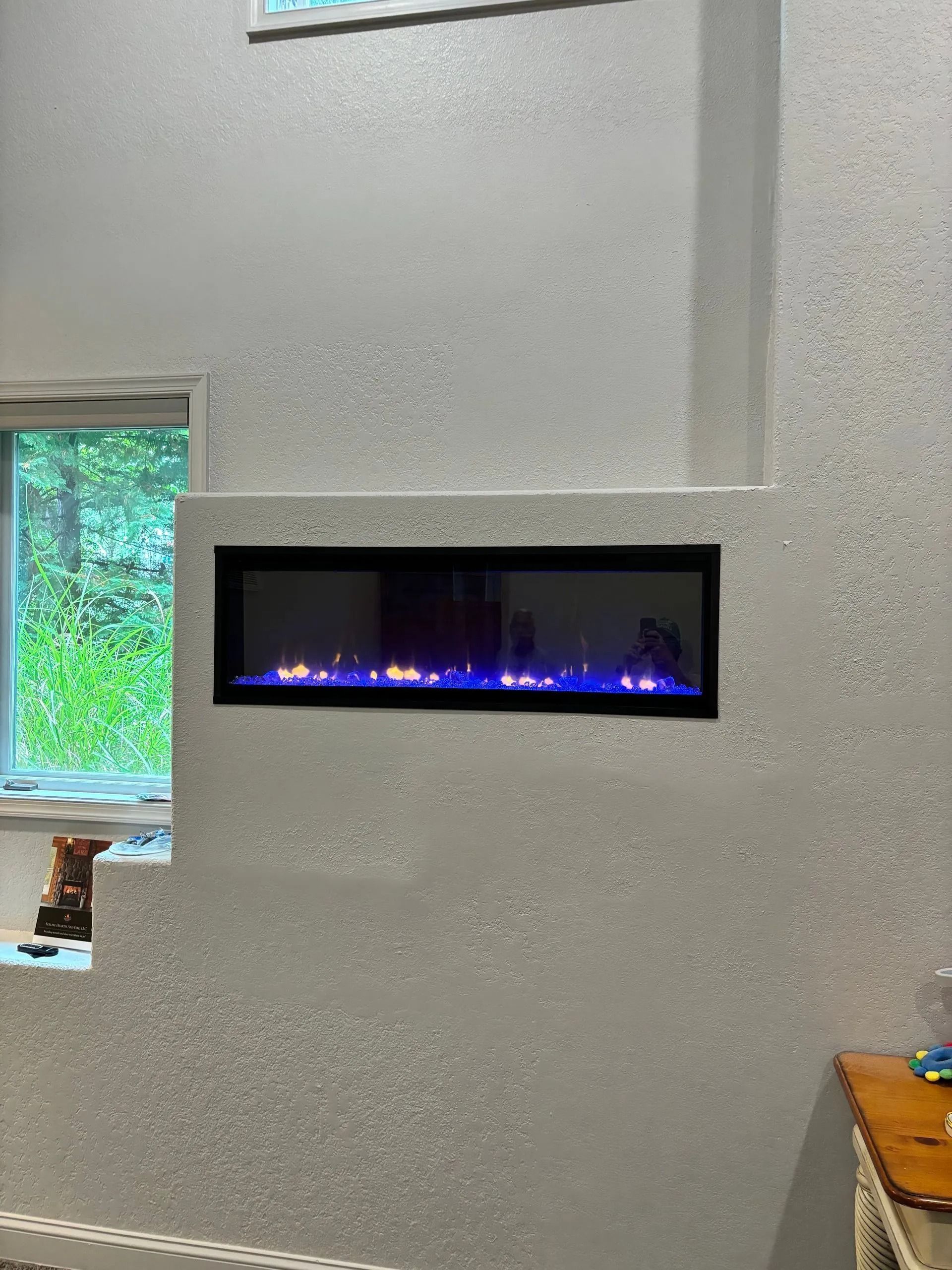 Electric fireplace built into a white textured wall with blue and orange flames.