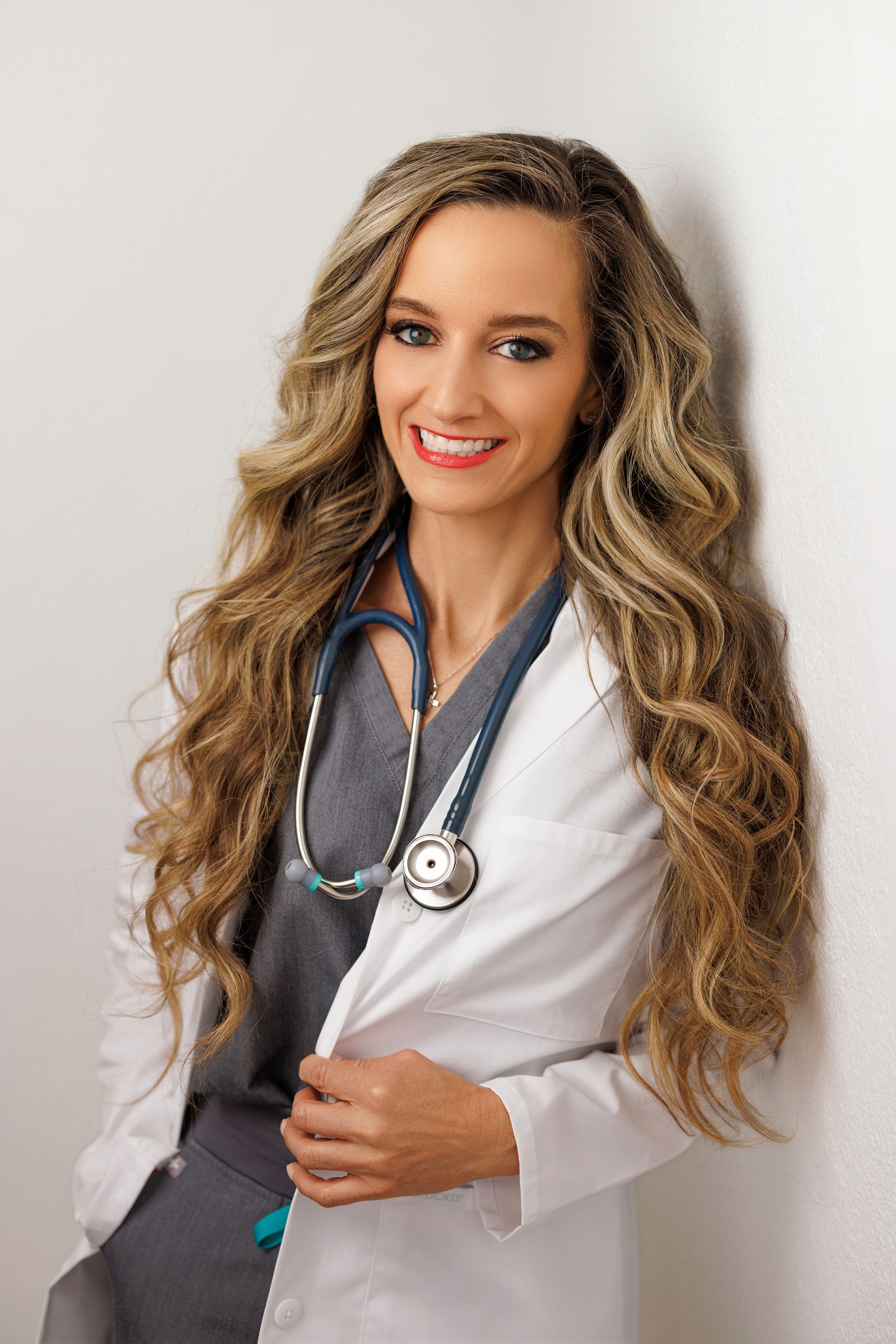 Smiling doctor in a white coat with a stethoscope, standing against a light background.