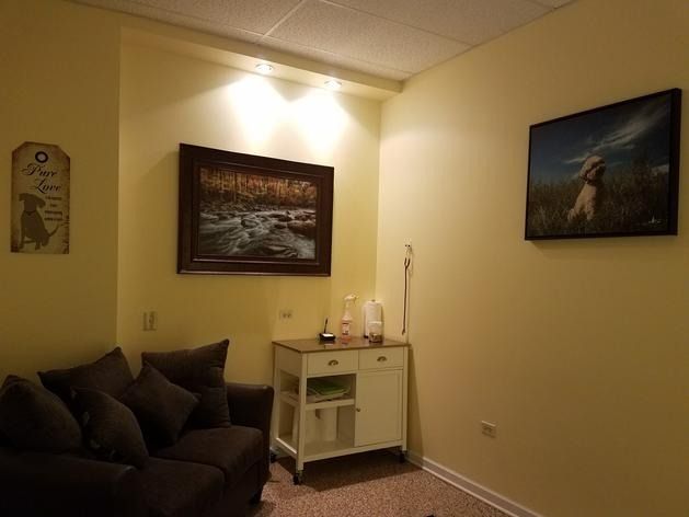 A cozy room with a dark sofa, a small white rolling cabinet, and two framed dog-themed artworks on pale yellow walls.