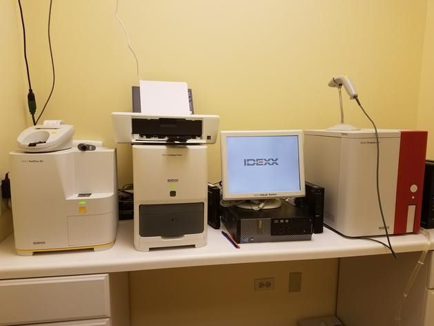 Laboratory equipment including analyzers, a computer, and a printer arranged on a white counter in a bright room.