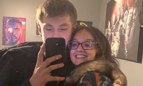 Two people smiling for a selfie in a bedroom, with posters on the wall.