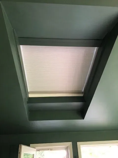 A rectangular skylight with white blinds in a teal-painted ceiling.
