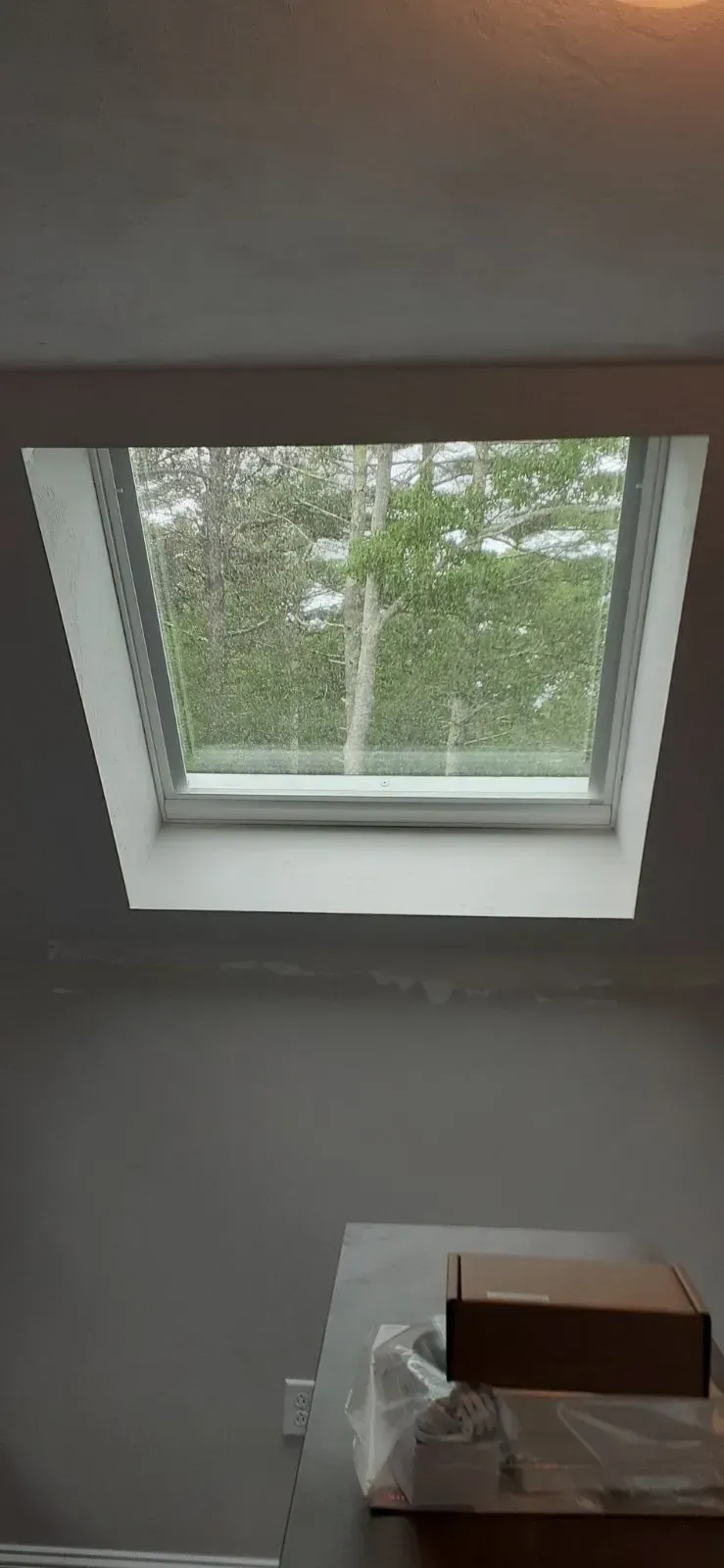 Skylight in a room with a view of green trees outside. A table with boxes is in the foreground.