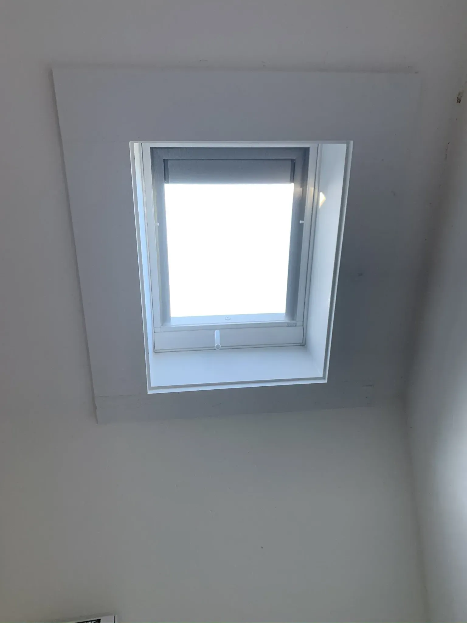 Skylight set in a white recessed ceiling. Light shines through window with a closed shade.