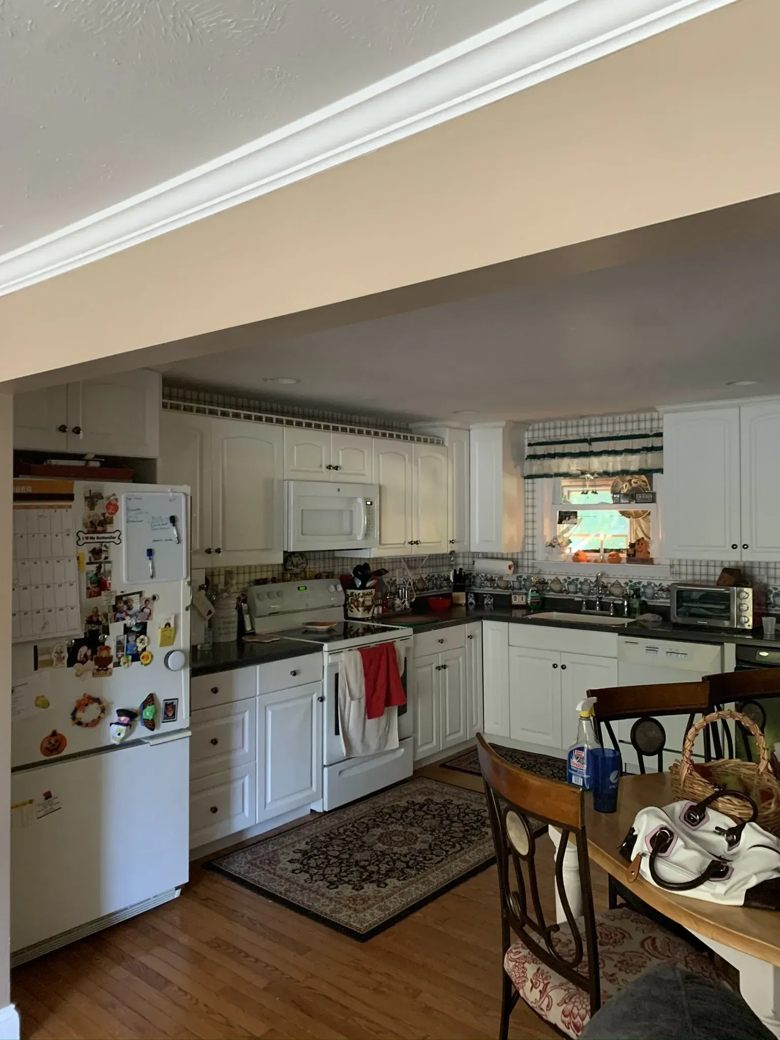 Kitchen with white cabinets, dark countertop, and wood floor. Includes refrigerator, appliances, and a dining table.