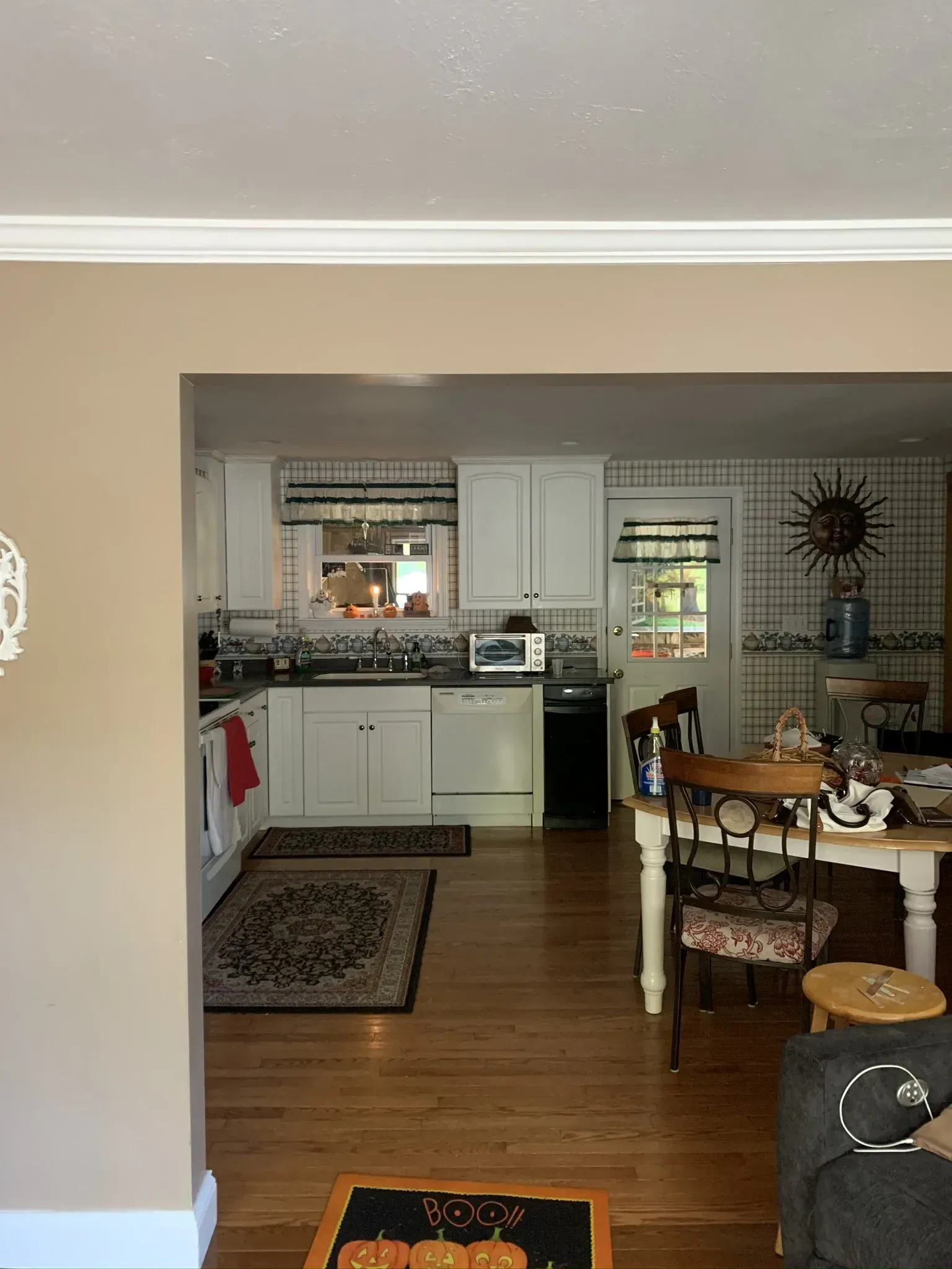 View into a kitchen with white cabinets, dark countertops, and hardwood floors. A dining table and chairs are in the foreground.