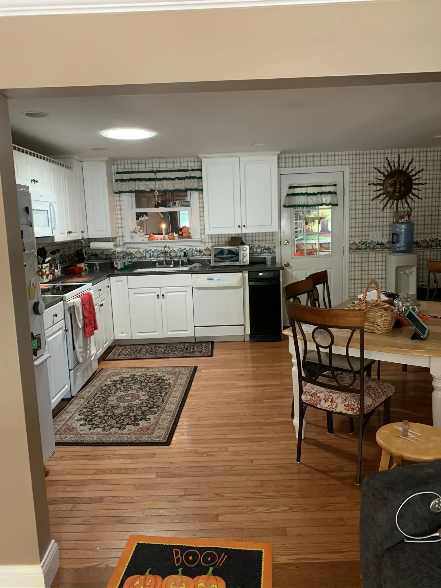 Kitchen with white cabinets, appliances, and wood flooring. A dining table with chairs is visible.