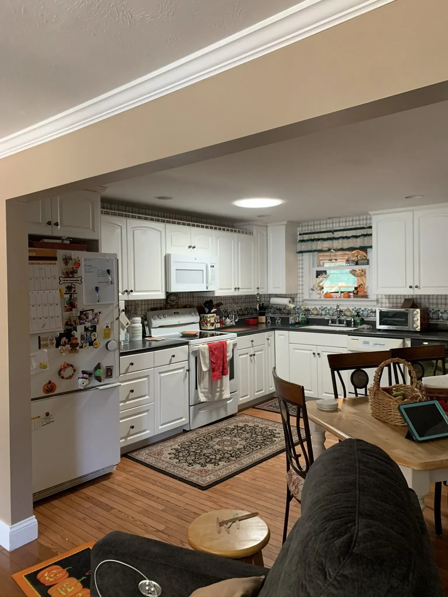 Kitchen with white cabinets, appliances, wooden floor, and a rug.