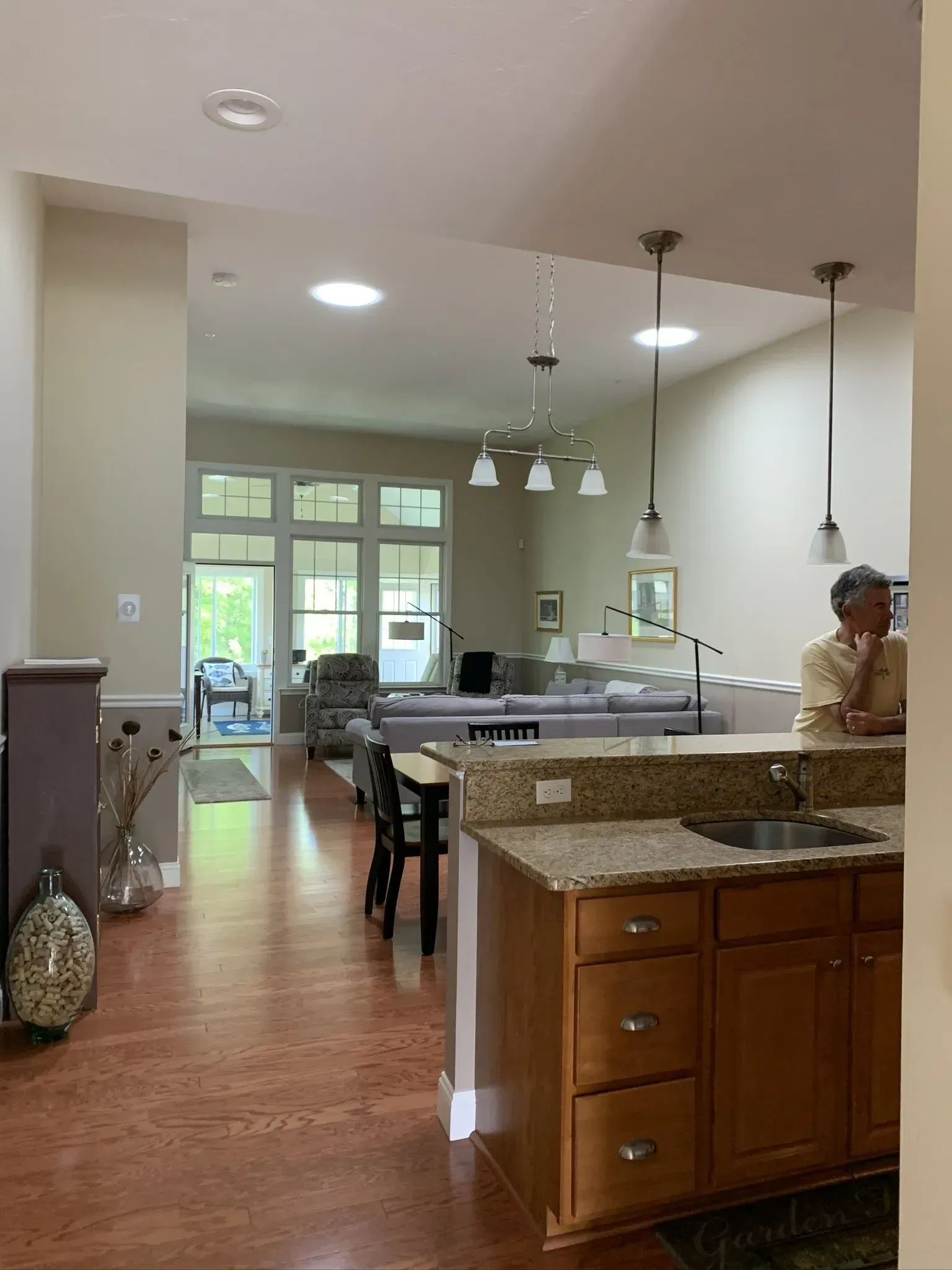 Open-concept kitchen and living area, person at counter. Cork flooring, granite counters, wood cabinets, skylights.