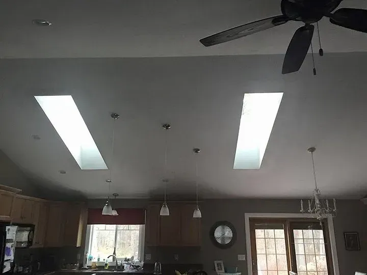 Kitchen ceiling with two rectangular skylights, pendant lights, and a ceiling fan.