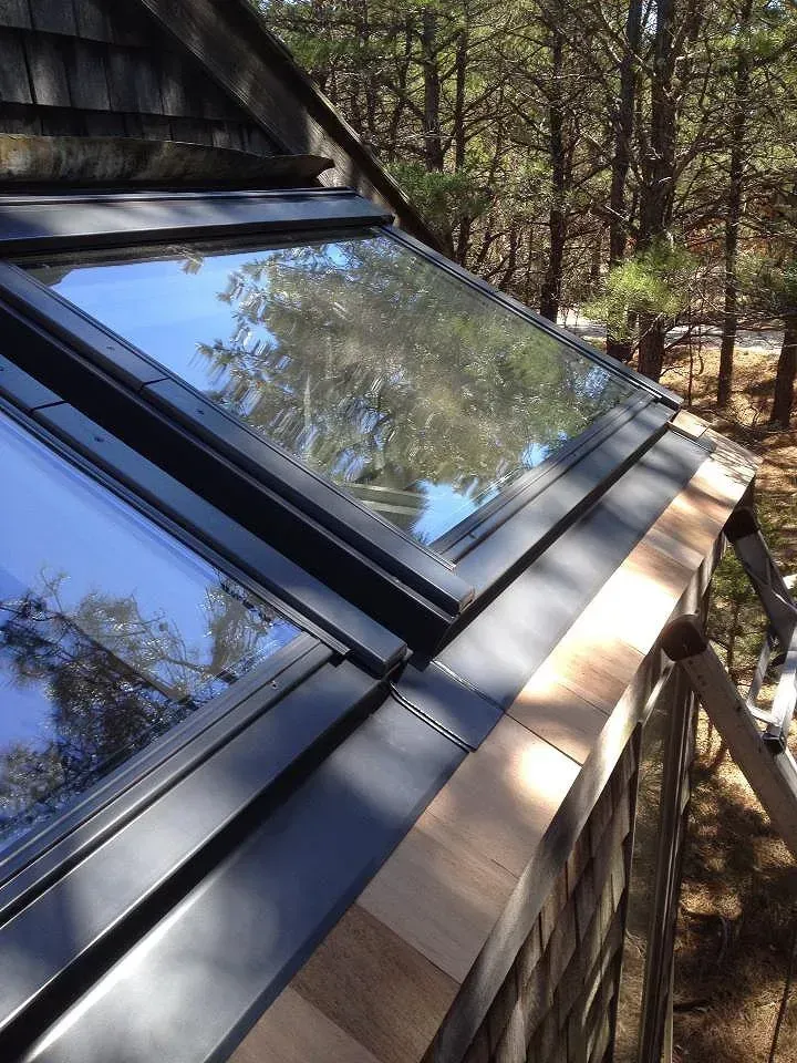 Angled skylights on a wood-shingled roof, set against a forest background.