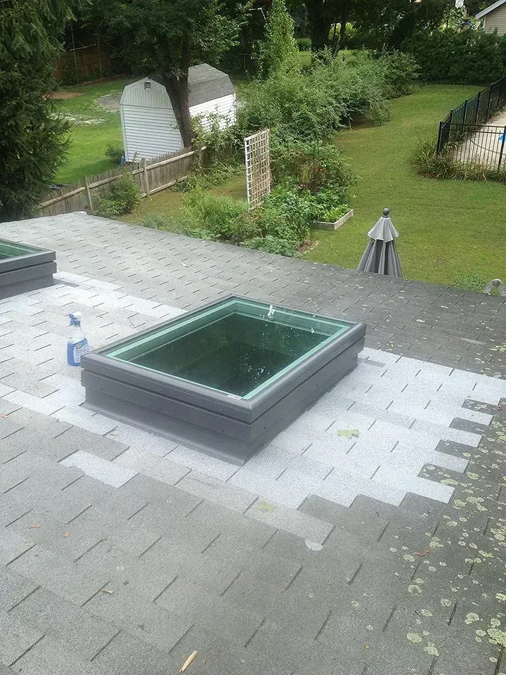 Skylight on a gray shingle roof, with backyard in background.