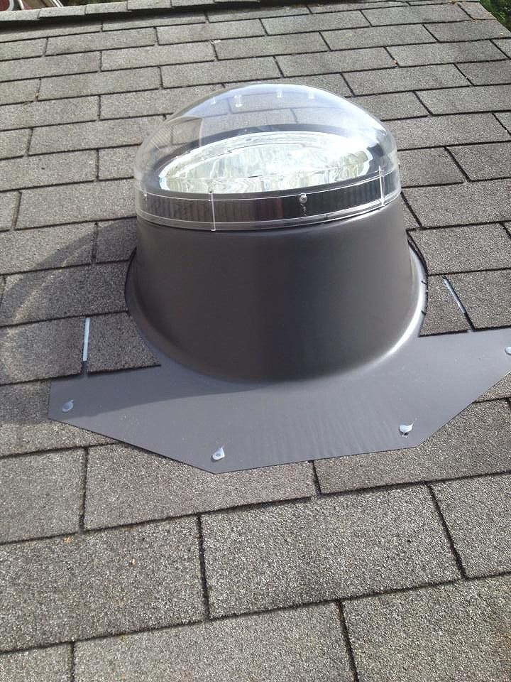 Skylight on a gray shingled roof, has a clear dome and metal flashing.
