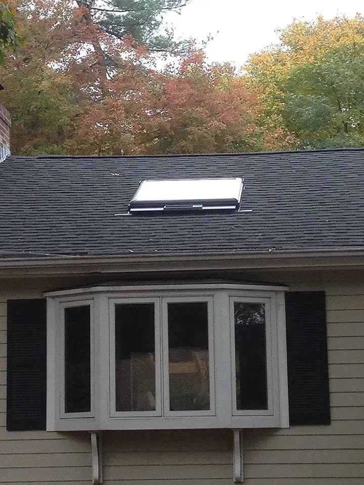 A house with a bay window and a skylight on the roof, set against colorful autumn trees.