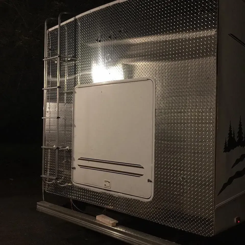 Silver camper with diamond plate siding, ladder, and white door.
