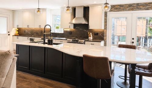 Bright modern kitchen with white island, black cabinets, pendant lights, and adjacent dining nook
