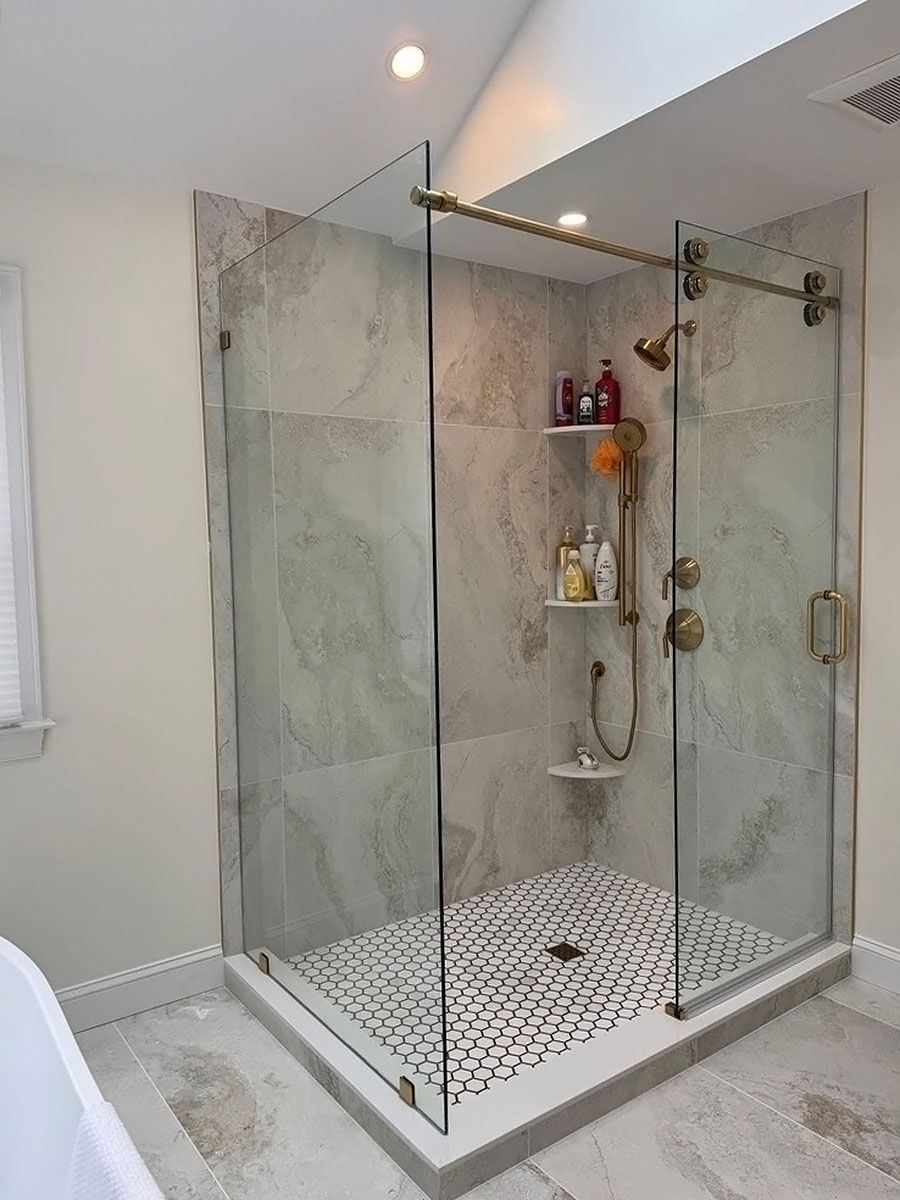 Modern walk-in shower with glass enclosure, marble tile walls, and hexagon mosaic floor in a bright bathroom