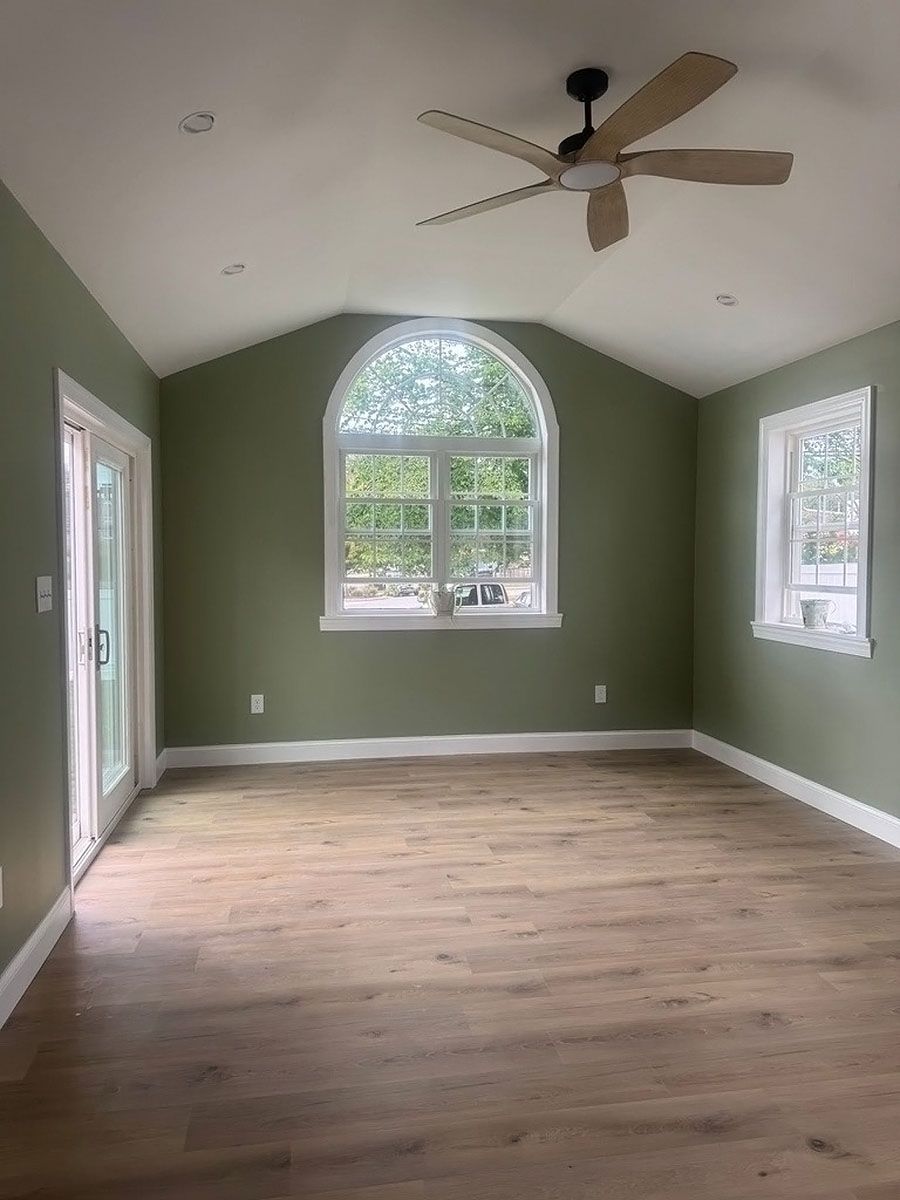 Empty room with green walls, wood floor, arched window, and ceiling fan.