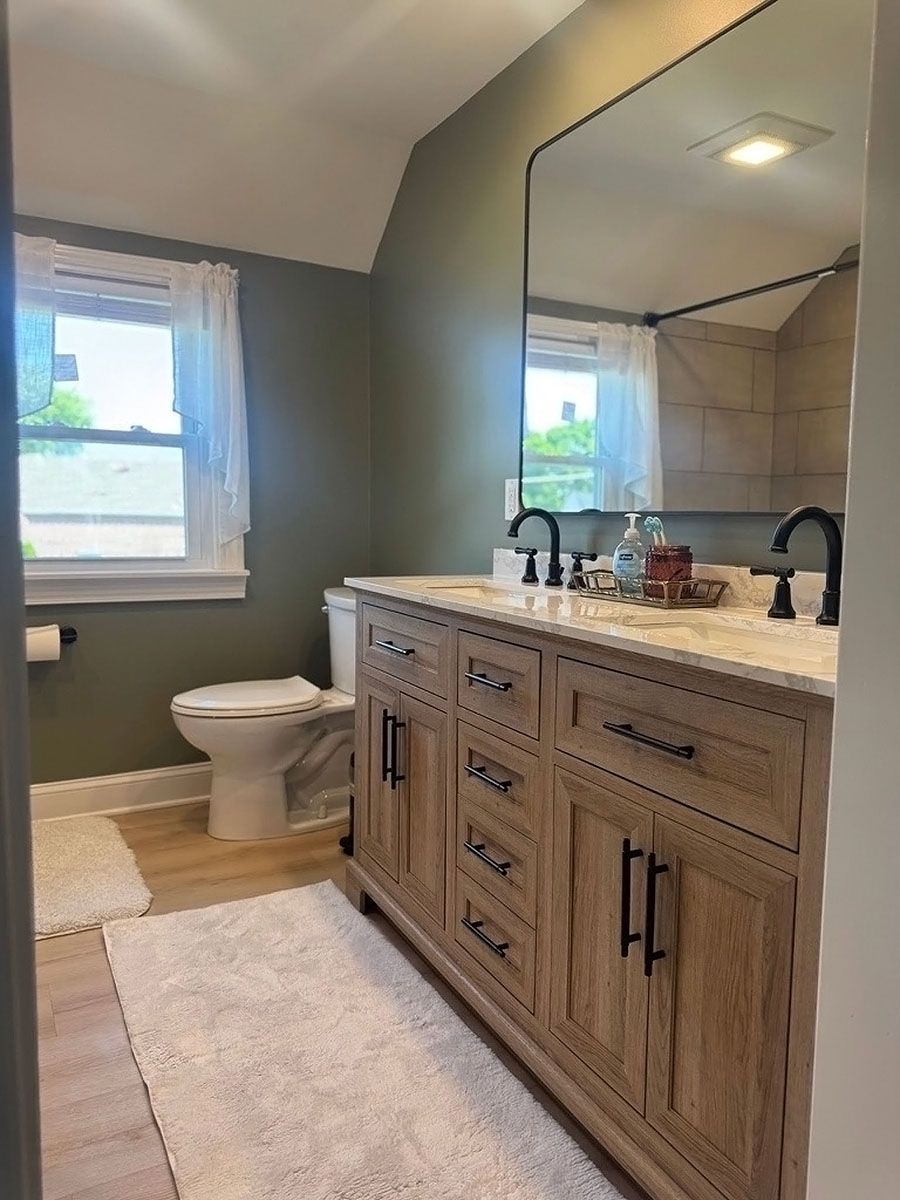Modern bathroom with wood vanity, large mirror, toilet, window, and soft neutral decor.