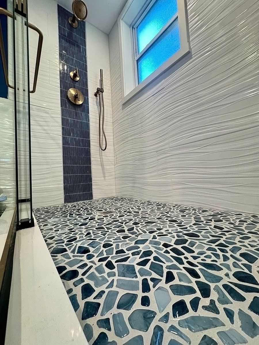 Modern bathroom shower with blue tile accent, white walls, mosaic floor, and a frosted window.
