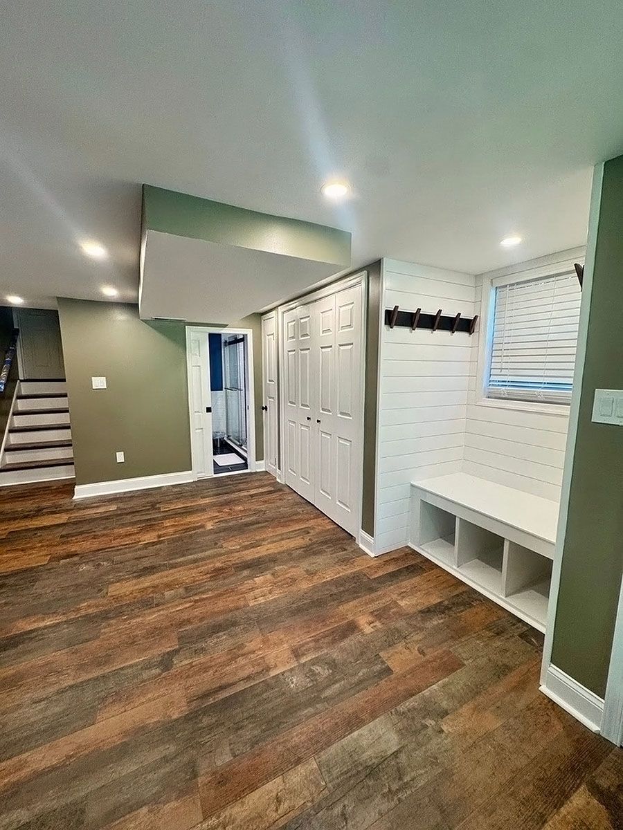 Empty entryway with wood-look flooring, white closets, green walls, and built-in bench and coat hooks.
